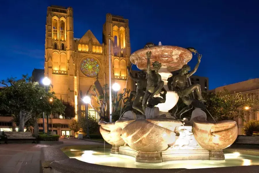 San Francisco's 格雷斯大教堂 is pictured at night with an ornate water fountain in the foreground.